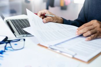 Foto: Person mit Dokumenten und Laptop